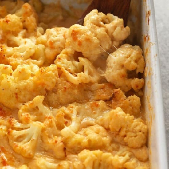 Cheesy cauliflower mac and cheese casserole in a baking dish with a wooden spoon.