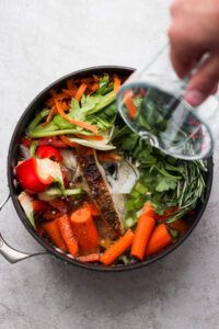 a person pouring liquid into a pan full of vegetables.