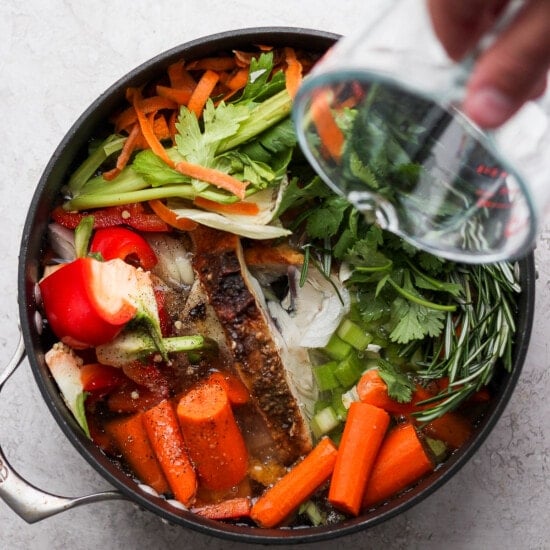 a person pouring liquid into a pan full of vegetables.