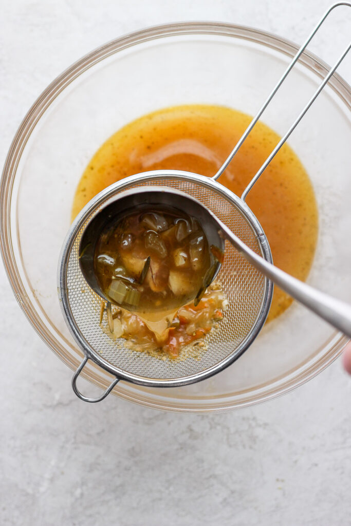 Pouring chicken broth through a sieve. 