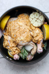 roasted whole chicken with lemons and herbs in a pan.