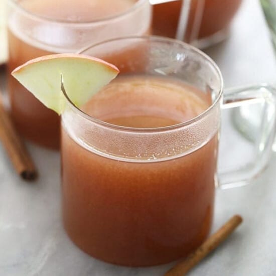 Two spiked mugs of apple cider with cinnamon sticks.