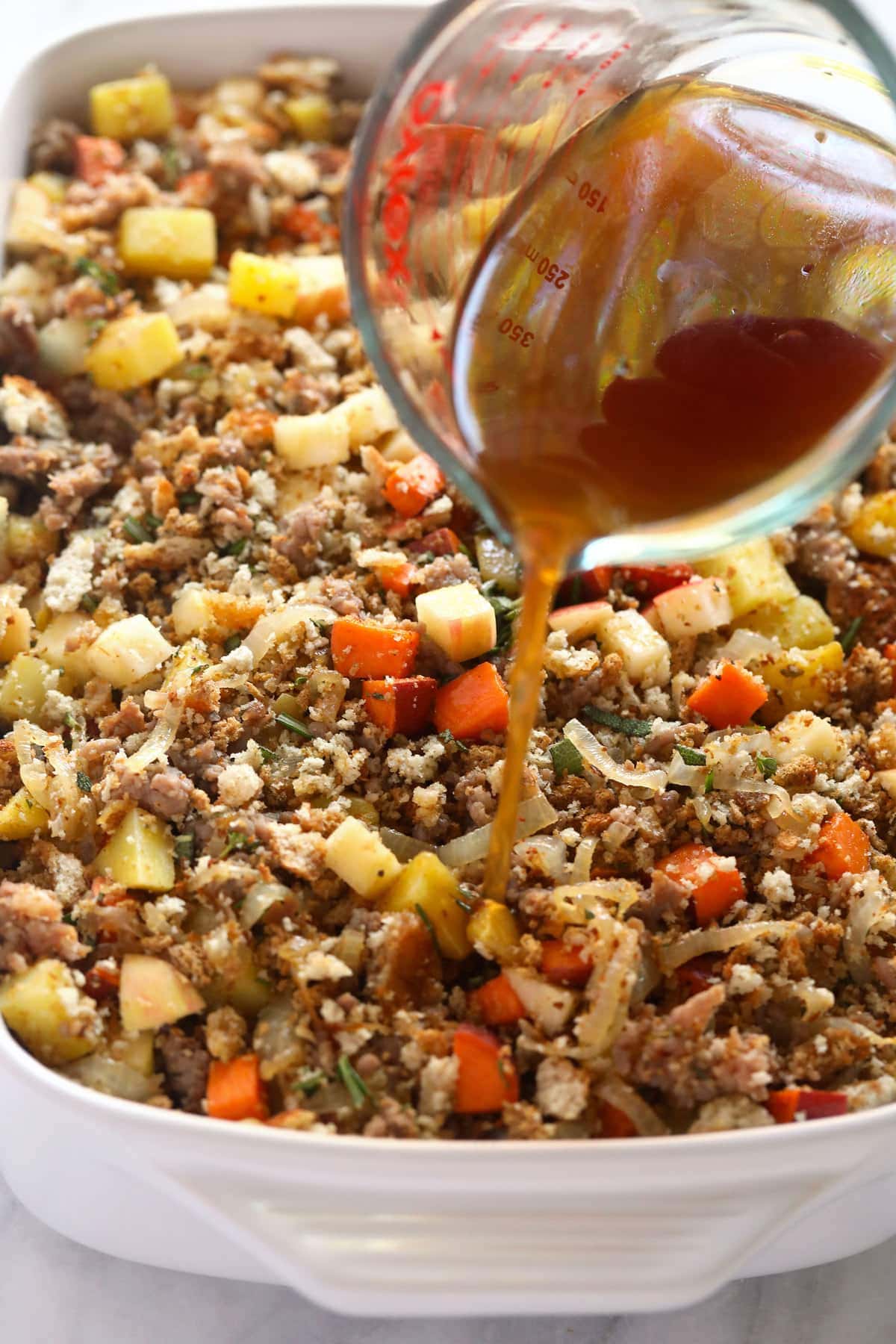 broth being poured over sausage stuffing before being baked