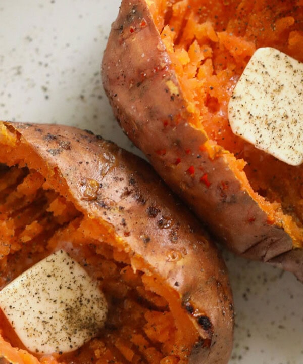 two roasted sweet potatoes with butter on a plate.