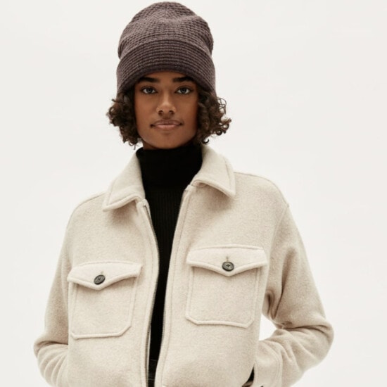 the model is wearing a beige jacket and a beanie.