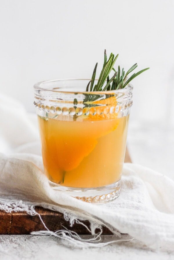a glass of orange juice with a sprig of rosemary.