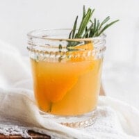 a glass of orange juice with rosemary sprigs.