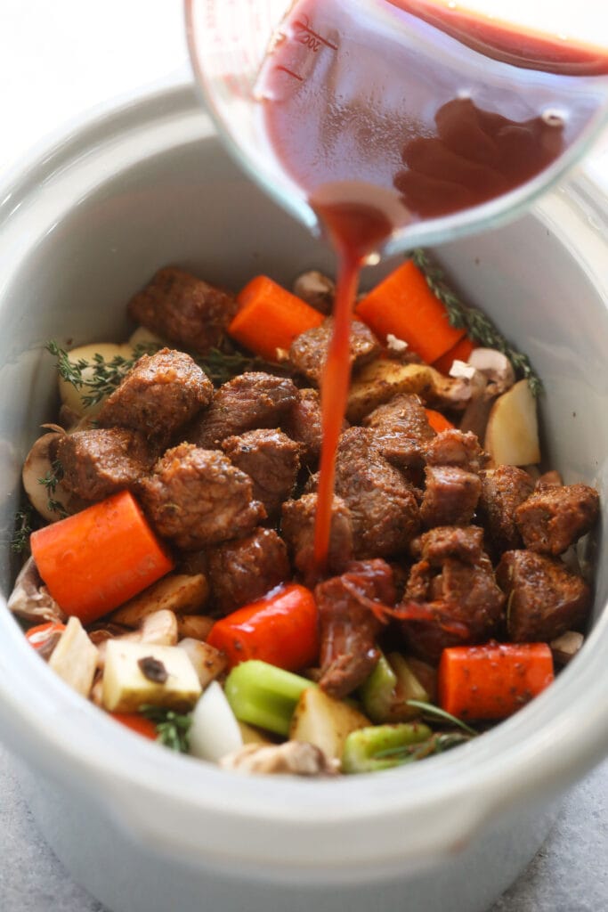 slow cooker beef stew ingredients being mixed together in a slow cooker