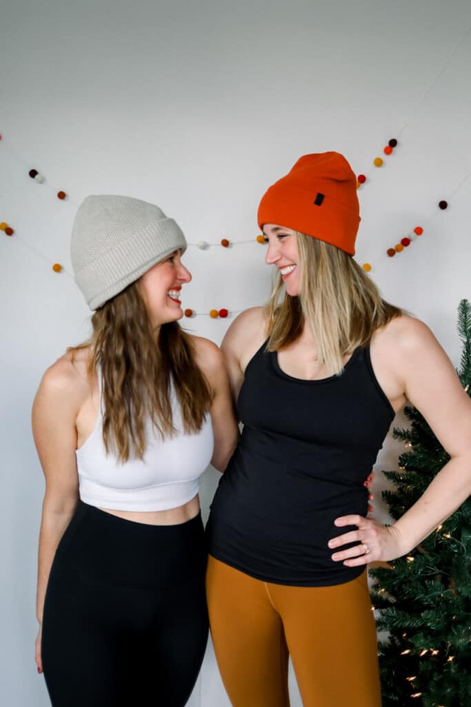 two women standing in front of a christmas tree wearing stocking caps