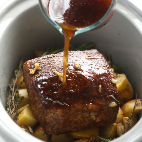 A slow cooker pork loin with potatoes, simmering in flavorful sauce.