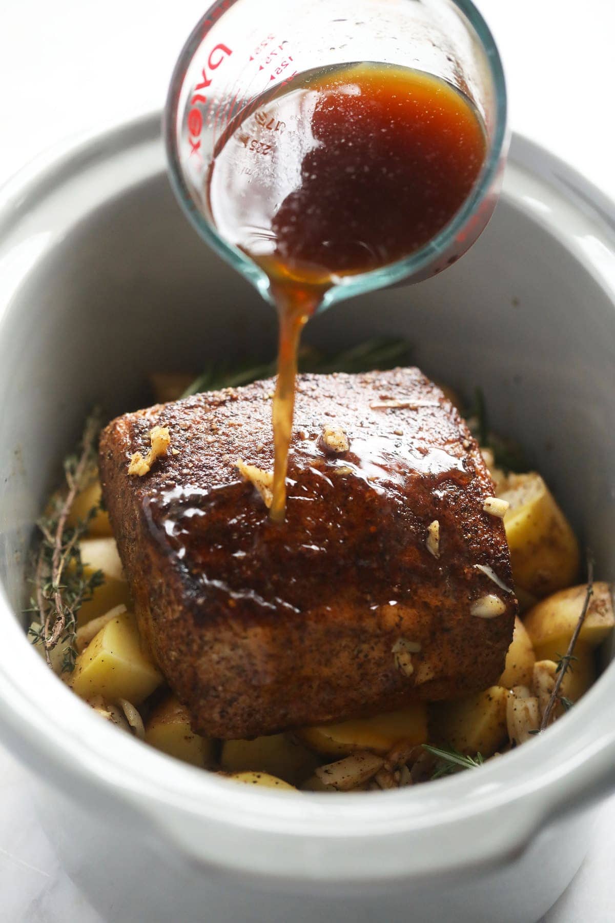 pork loin roast on a bed of potatoes being placed in a slow cooker.