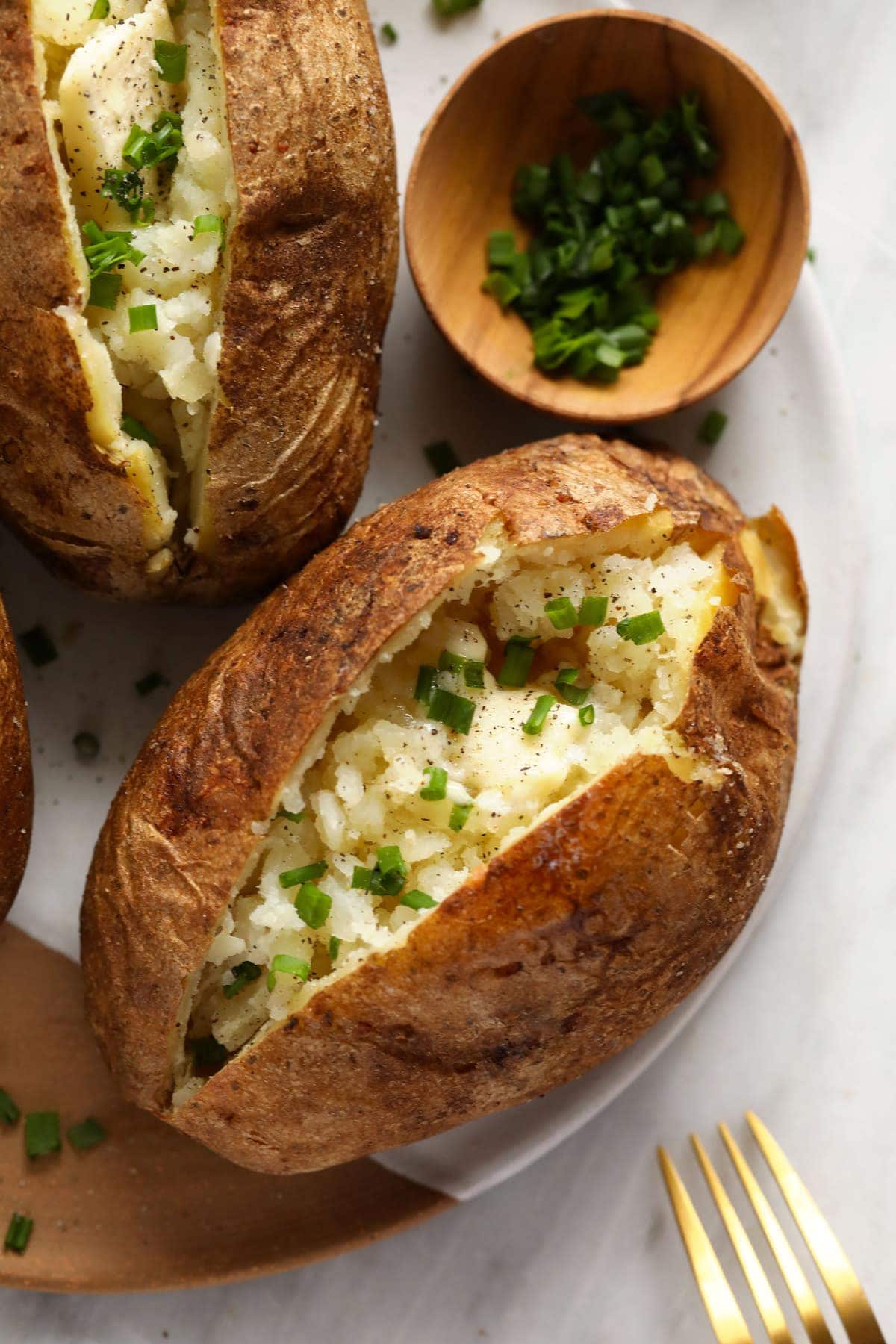 Baked potatoes on a plate with butter, salt, pepper, and chives.