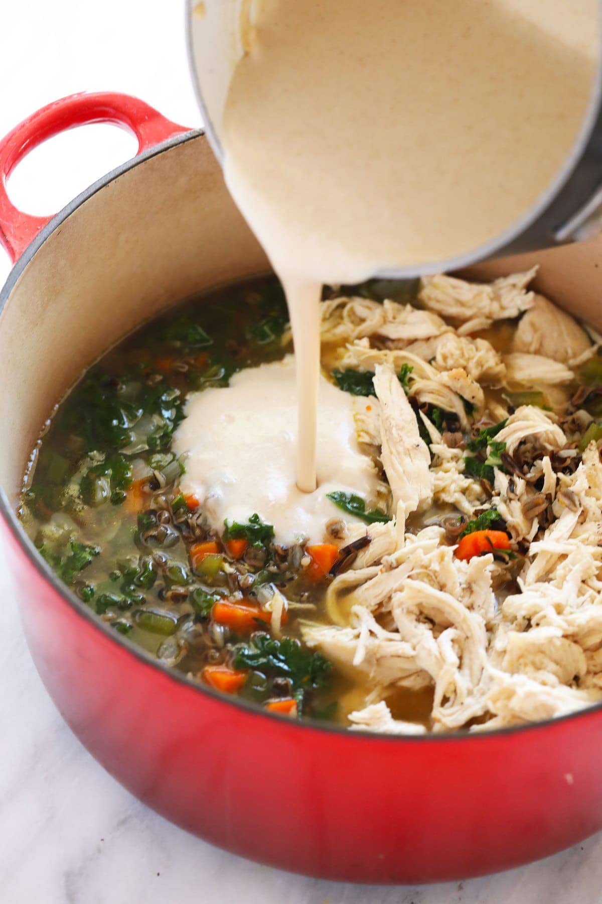 Roux being poured into chicken wild rice soup to make it creamy.