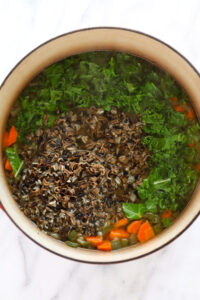 a chicken and wild rice soup with carrots and greens in it.