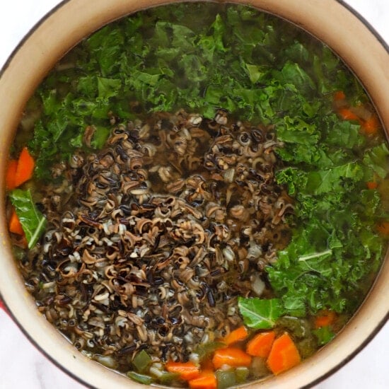 a chicken and wild rice soup with carrots and greens in it.