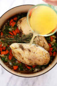 a person pouring olive oil into a pan with vegetables to prepare chicken wild rice soup.