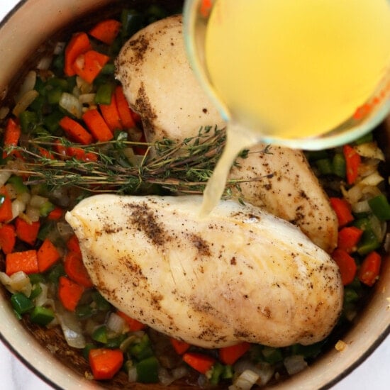 a person pouring olive oil into a pan with vegetables to prepare chicken wild rice soup.