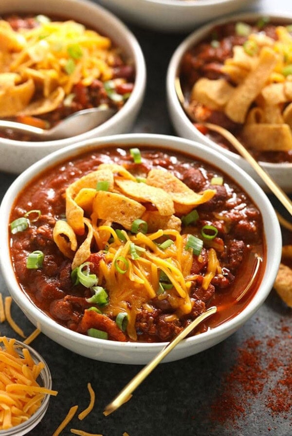 four bowls of chili with cheese and tortilla chips.