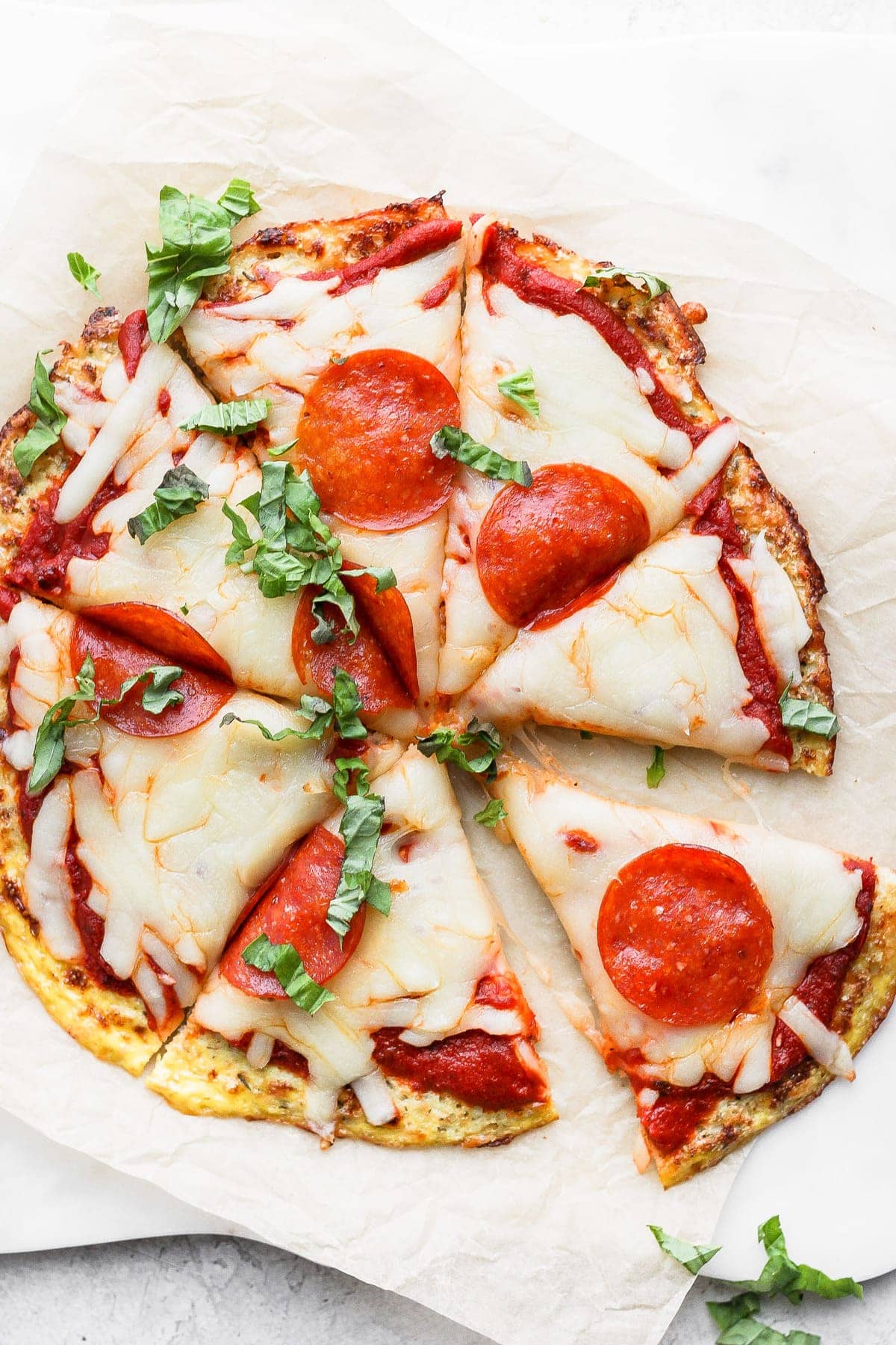 Cauliflower pizza crust topped with cheese, pepperoni, and fresh basil. 