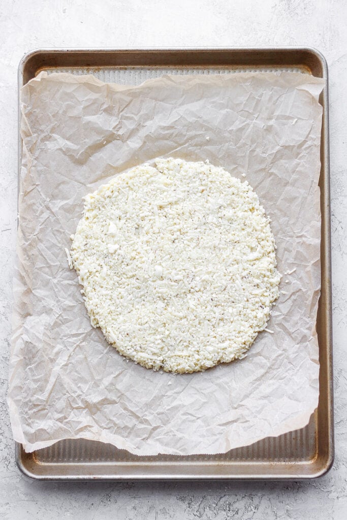 Cauliflower pizza crust made into a circle on a baking sheet. 