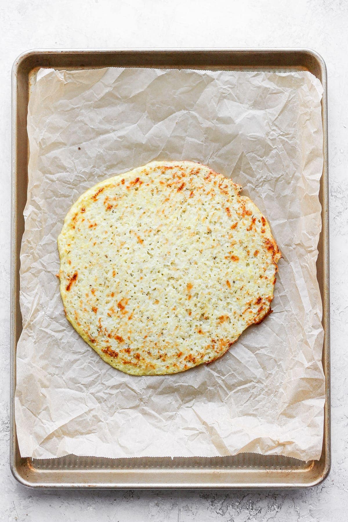 Golden cauliflower pizza crust on parchment paper. 