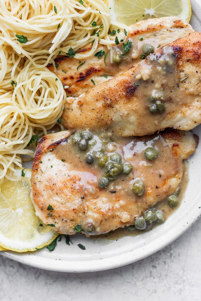 Chicken piccata on a plate with capers on top/ 