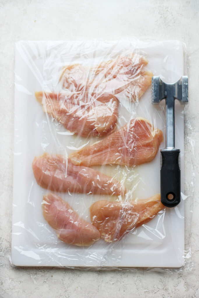 Pounding chicken breast on a cutting board with a meat cleaver. 