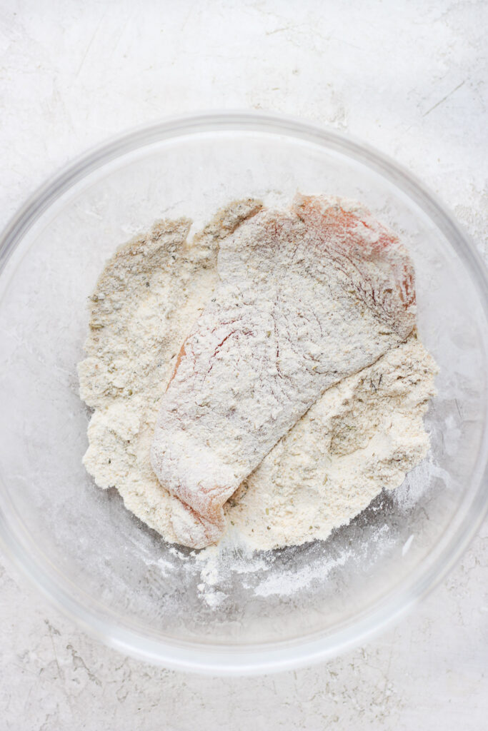 raw chicken breast being dredged in seasonings and flour