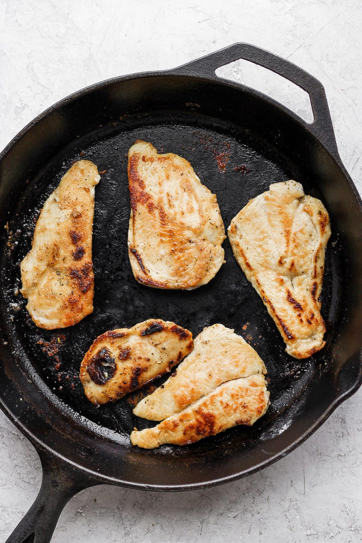 chicken breasts being seared in a cast iron skillet for chicken marsala