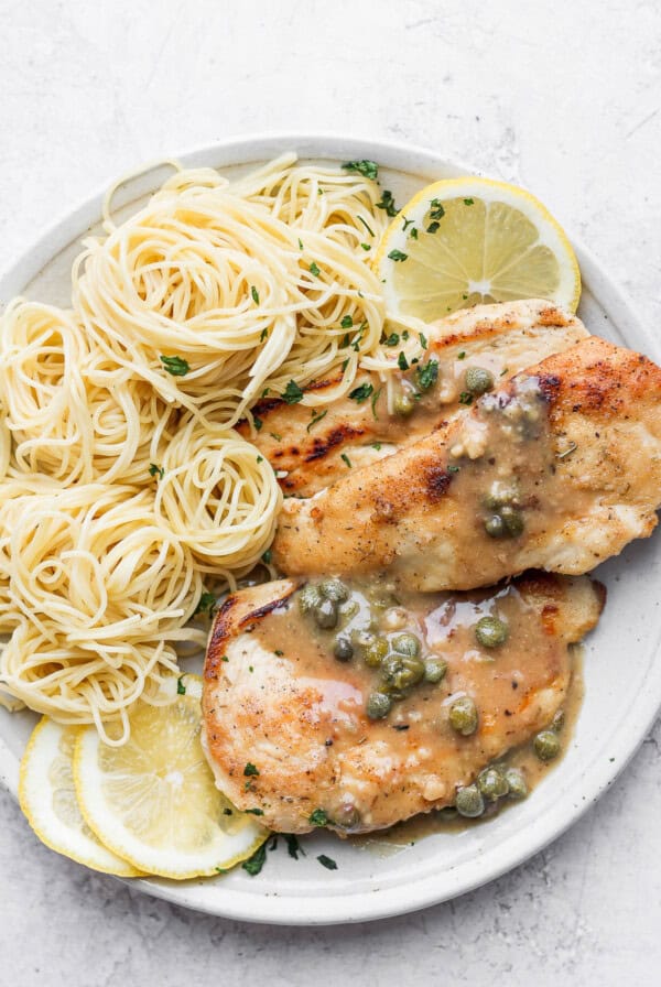 a plate with chicken breasts, pasta and lemon sauce.