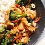 A plate with ginger chicken stir-fry, featuring broccoli, carrots, and cashews next to white rice.