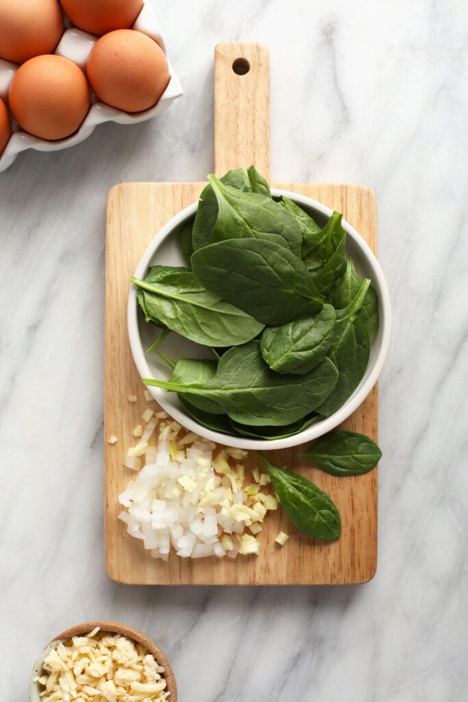 Spinach, onion, and garlic on a small cutting board. 