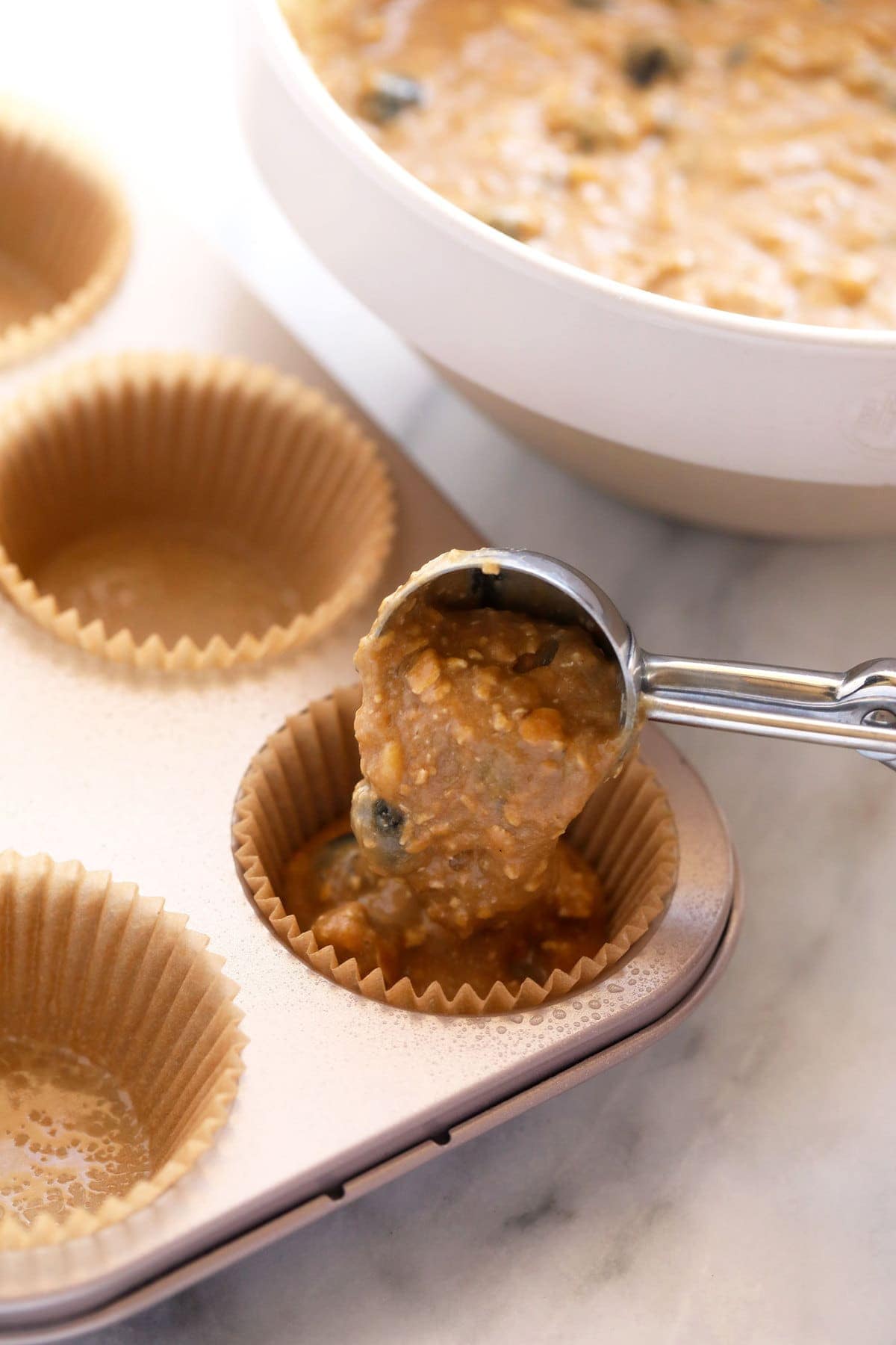 blueberry muffin batter being poured into muffin liners in a muffin tin