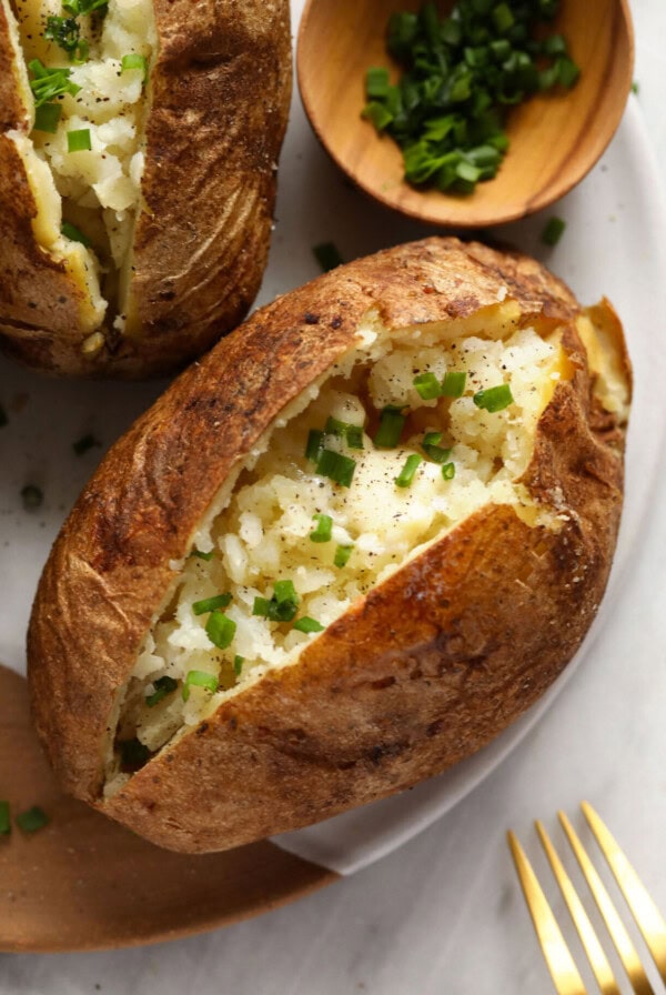 three baked potatoes with chives on a plate.