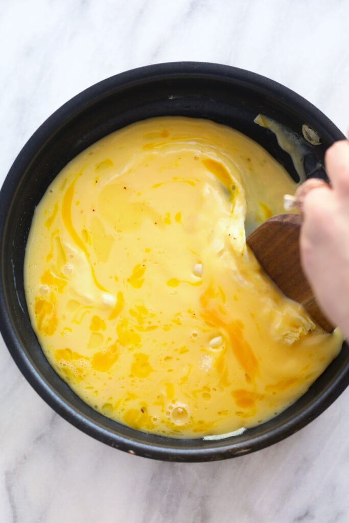 scrambled eggs in a non stick pan being cooked over medium heat and stirred with a wooden spatula