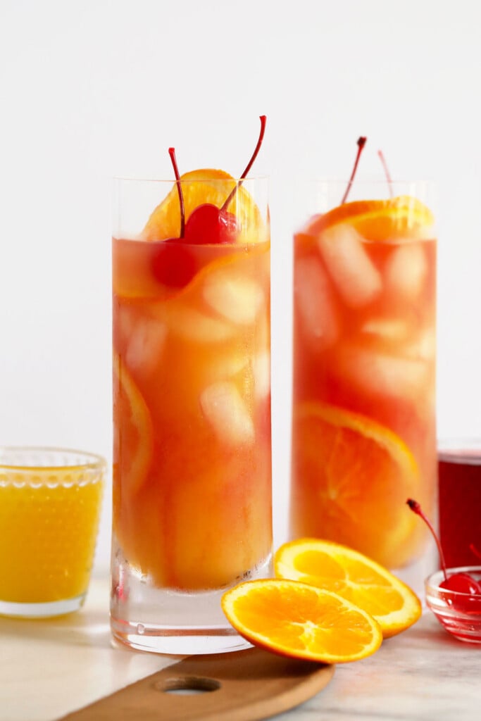 two glasses of orange juice with ice and orange slices.