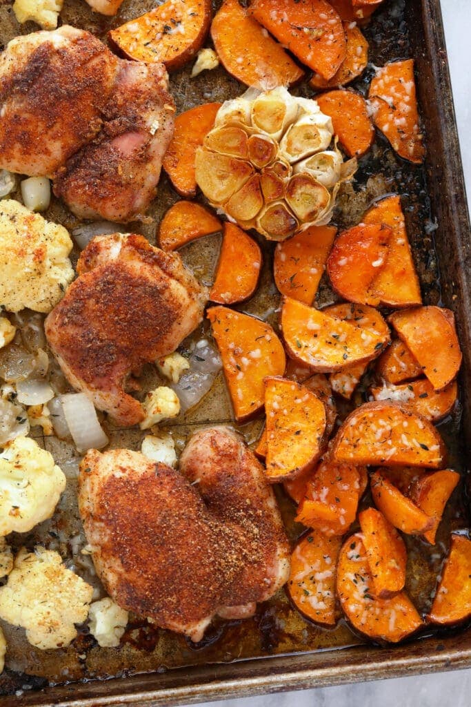 Chicken, sweet potatoes, cauliflower, onion, and garlic on a baking sheet. 