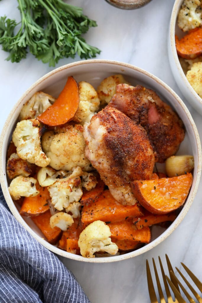 Chicken thighs, cauliflower, and sweet potatoes in a bowl. 