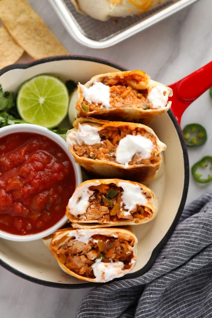shredded chicken burritos cut in half and displayed with a bowl of salsa.
