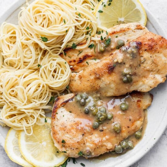 Chicken piccata on a plate with angel hair pasta.