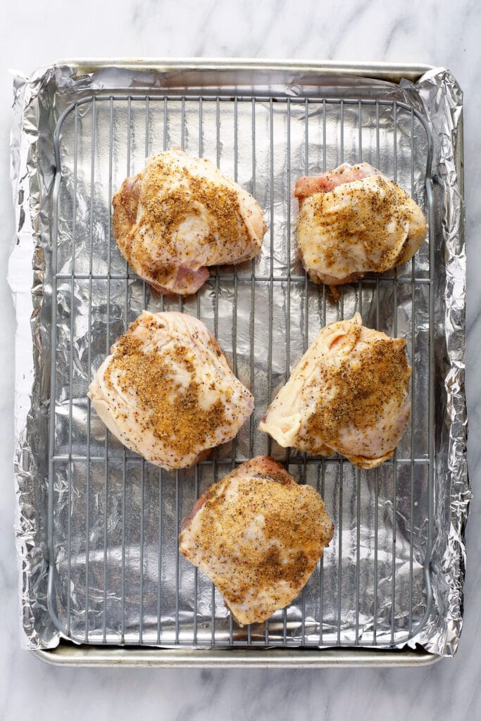 Chicken thighs on a baking sheet with seasonings. 