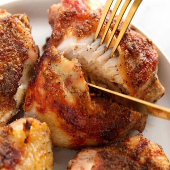 close up of baked chicken thigh being cut into with a gold knife and fork