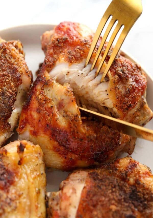 close up of baked chicken thigh being cut into with a gold knife and fork