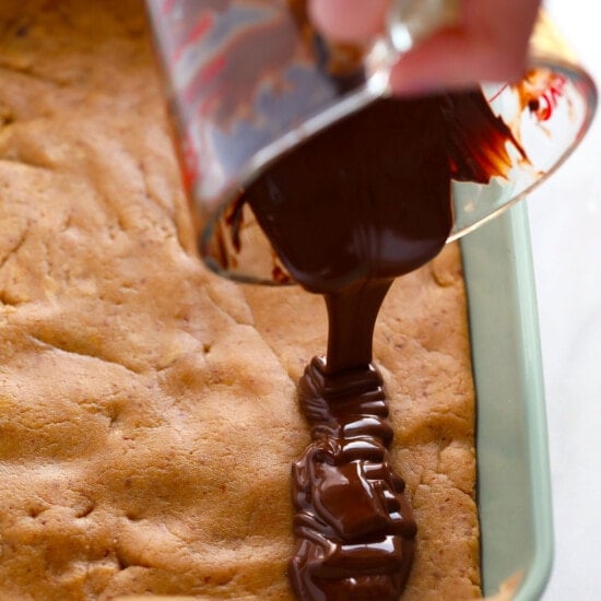 a person drizzling chocolate over a peanut butter protein bar in a pan.