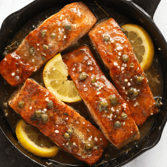 Salmon fillets in a skillet with lemon slices.