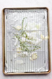 herbs and onion under metal rack on baking sheet.