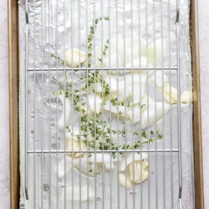 herbs and onion under metal rack on baking sheet.