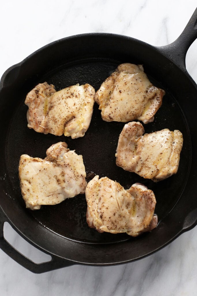 boneless skinless chicken thighs being seared in a cast iron skillet