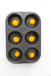 Baked eggs in the oven using a muffin tin, on a white background.