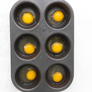 Baked eggs in the oven using a muffin tin, on a white background.